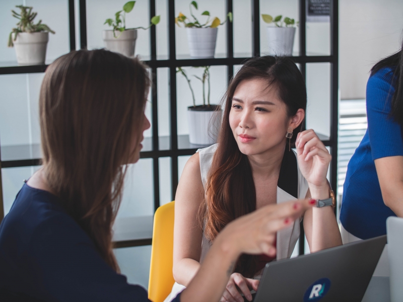 conversation between colleagues in the office 2 women having a conversation, one is Asian